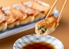 焼きあがった「しそ餃子」を箸で1粒持ち上げ、器に入ったポン酢につけている食べ方イメージ。さわやかな大葉とポン酢が絶妙にマッチする。