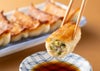 焼きあがった「将軍餃子」または「しそ餃子」を箸で1粒持ち上げ、器に入ったポン酢につけている食べ方イメージ。大分県産ブランド豚「米の恵み」を使用した贅沢な味わい。