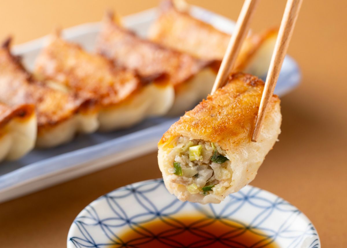 焼きあがった「将軍餃子」または「しそ餃子」を箸で1粒持ち上げ、器に入ったポン酢につけている食べ方イメージ。大分県産ブランド豚「米の恵み」を使用した贅沢な味わい。