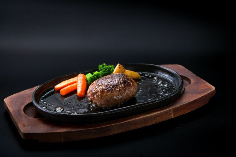 大分県のブランド牛「おおいた和牛（黒毛和牛）」を贅沢に使用したハンバーグの調理後の盛り付け画像。鉄板の上で肉汁が溢れるハンバーグに野菜を添えた、豪華なディナーイメージ。