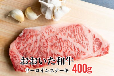 大分県のブランド牛「おおいた和牛（黒毛和牛）」のサーロインステーキ肉を、ニンニクと共にまな板に置いた調理前のイメージ画像。美しい霜降りと厚みのある高級ステーキ。