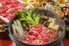 大分県産「おおいた和牛（黒毛和牛）」のロース肉または赤身肉を、野菜と共に鍋で煮込み、すき焼きにしている調理中の画像。甘い割り下の香りが漂う、食卓を囲むのに最適な贅沢な鍋料理。
