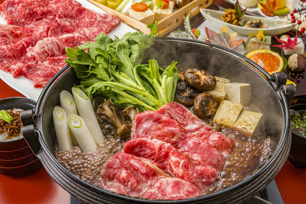 大分県産「おおいた和牛（黒毛和牛）」のロース肉または赤身肉を、野菜と共に鍋で煮込み、すき焼きにしている調理中の画像。甘い割り下の香りが漂う、食卓を囲むのに最適な贅沢な鍋料理。