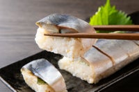 大分県産の「関さば棒寿司」（冷凍）を切って、一切れを箸で持ち上げたアップ画像。身の締まった関さばとシャリのバランスが伝わる、お取り寄せ寿司。