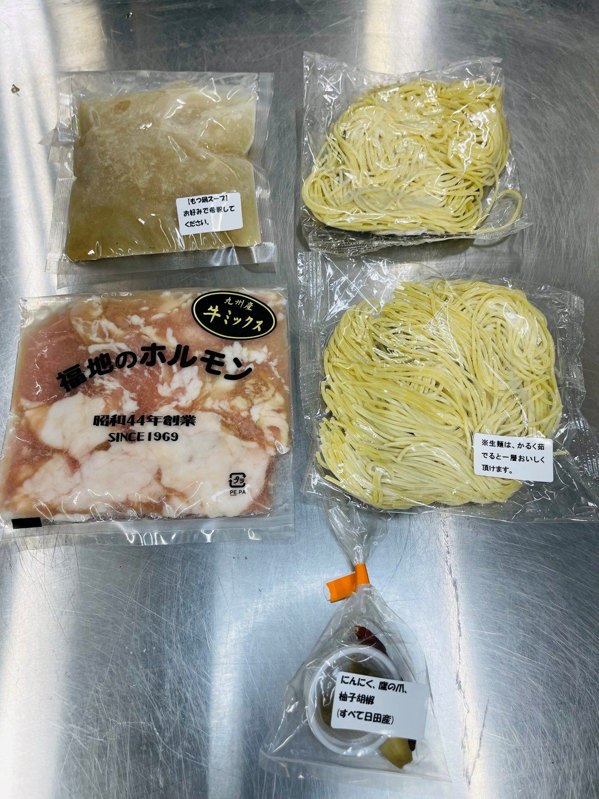 【福地のうなるホルモン】もつ鍋セットの、もつ、特製スープ、麺、薬味のパックを個別に並べた内容量画像。ご自宅で簡単に調理できる、専門店の味が楽しめるセット。