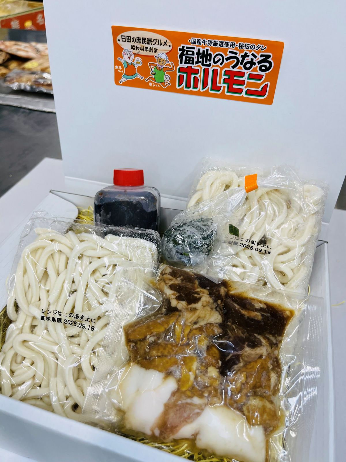 焼きうどんの麺、特製タレ、ホルモン、ネギがセットで入った「焼きうどんセット（2人前）」の箱入り内容量画像。ご自宅用はもちろん、お土産にも最適なセット。