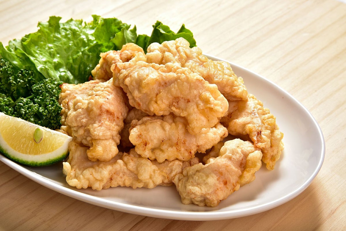 大分名物「とり天」を皿に盛り付け、かぼすを添えた画像。外はサクサク、中はジューシーな大分のご当地グルメの調理例。