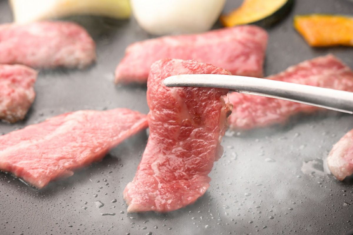 大分県産「おおいた和牛」の肉を鉄板または網で焼いている調理中の画像。上質な脂がジュージューと音を立てて溶け出し、食欲をそそる高級焼肉風景。