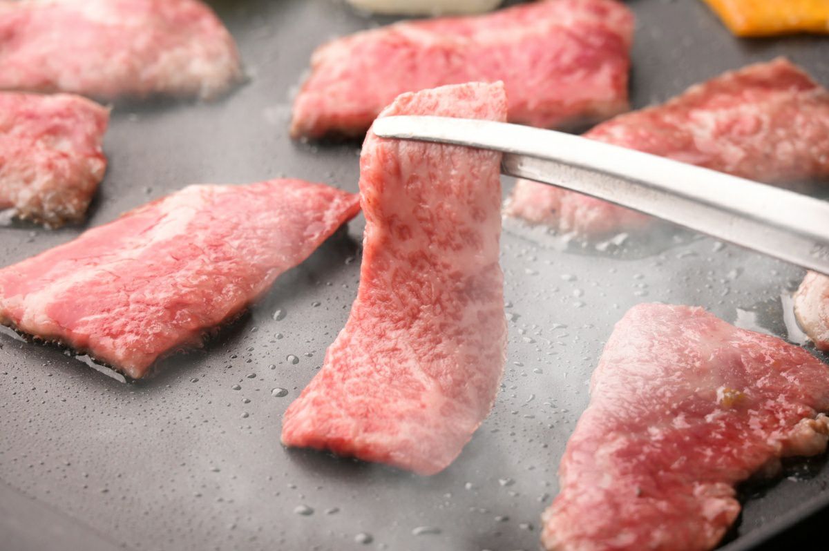 大分県のブランド牛「おおいた和牛」の霜降り肉を鉄板または網で焼いている調理中の画像。高級和牛の豊かな旨みが溶け出し、食欲をそそる焼肉風景。