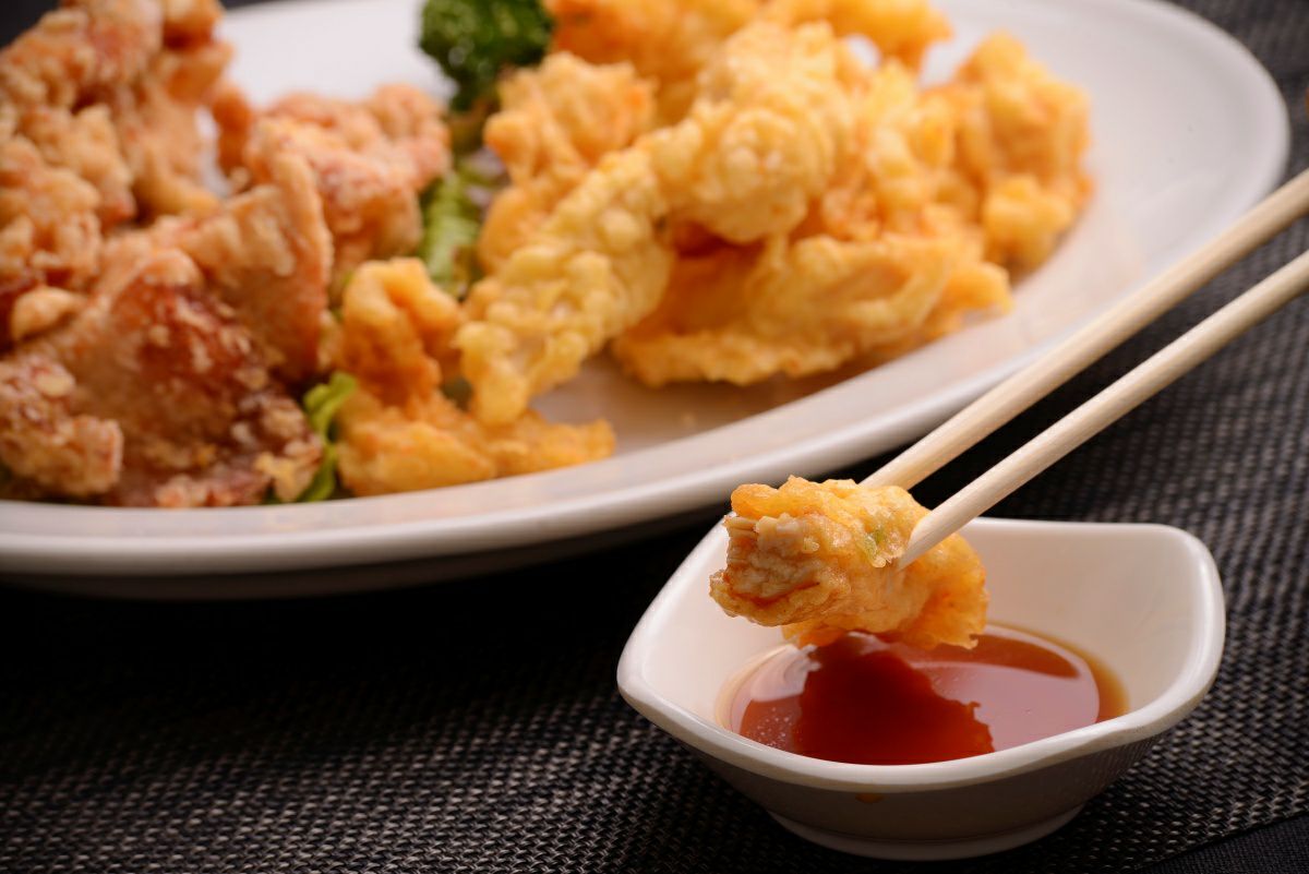 揚がったばかりの大分名物「とり天」を、箸で持ち上げ、特製ポン酢につけているアップ画像。揚げたてのサクサク食感が伝わる、大分のお取り寄せグルメ。