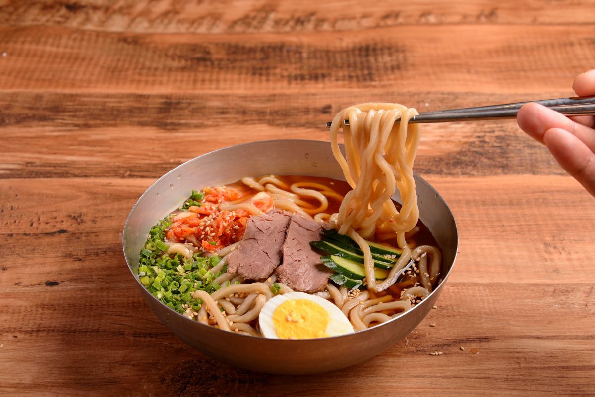 「別府冷麺」のコシのある太麺を箸で持ち上げている食べ方イメージ画像。冷たいスープと特製チャーシュー、キムチと共に食欲をそそる。