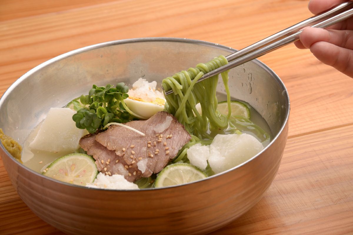 大分名物「かぼす冷麺」の麺を箸で持ち上げている食べ方イメージ画像。かぼすの爽やかなスープが絡む、つるつるとした食感の冷麺。