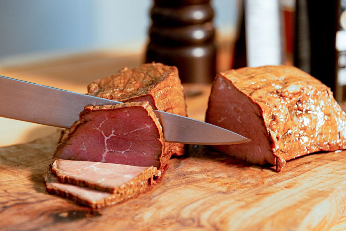 「かぼす冷麺」に添えるチャーシューを、まな板の上で包丁で丁寧にスライスしている調理工程の画像。特製チャーシューを手作りで用意している様子。