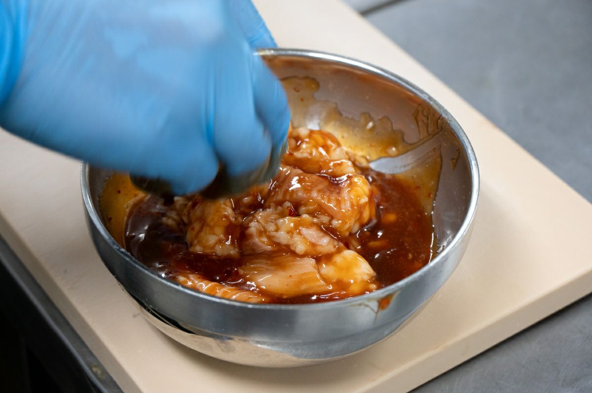 新鮮なホルモンを、特製の秘伝のタレに絡めている調理前の画像。丼の具の濃厚な旨味の元となる、タレ漬けの工程。