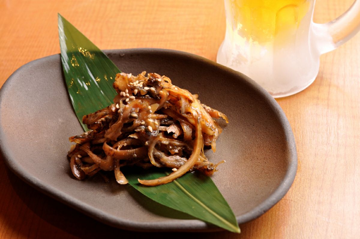 特製の甘辛いタレで味付けされた「鶏皮炭火焼」を皿に盛り付けた画像。香ばしい炭火の風味と、カリッと焼けた鶏皮の食感が伝わる、おつまみに最適な一品。