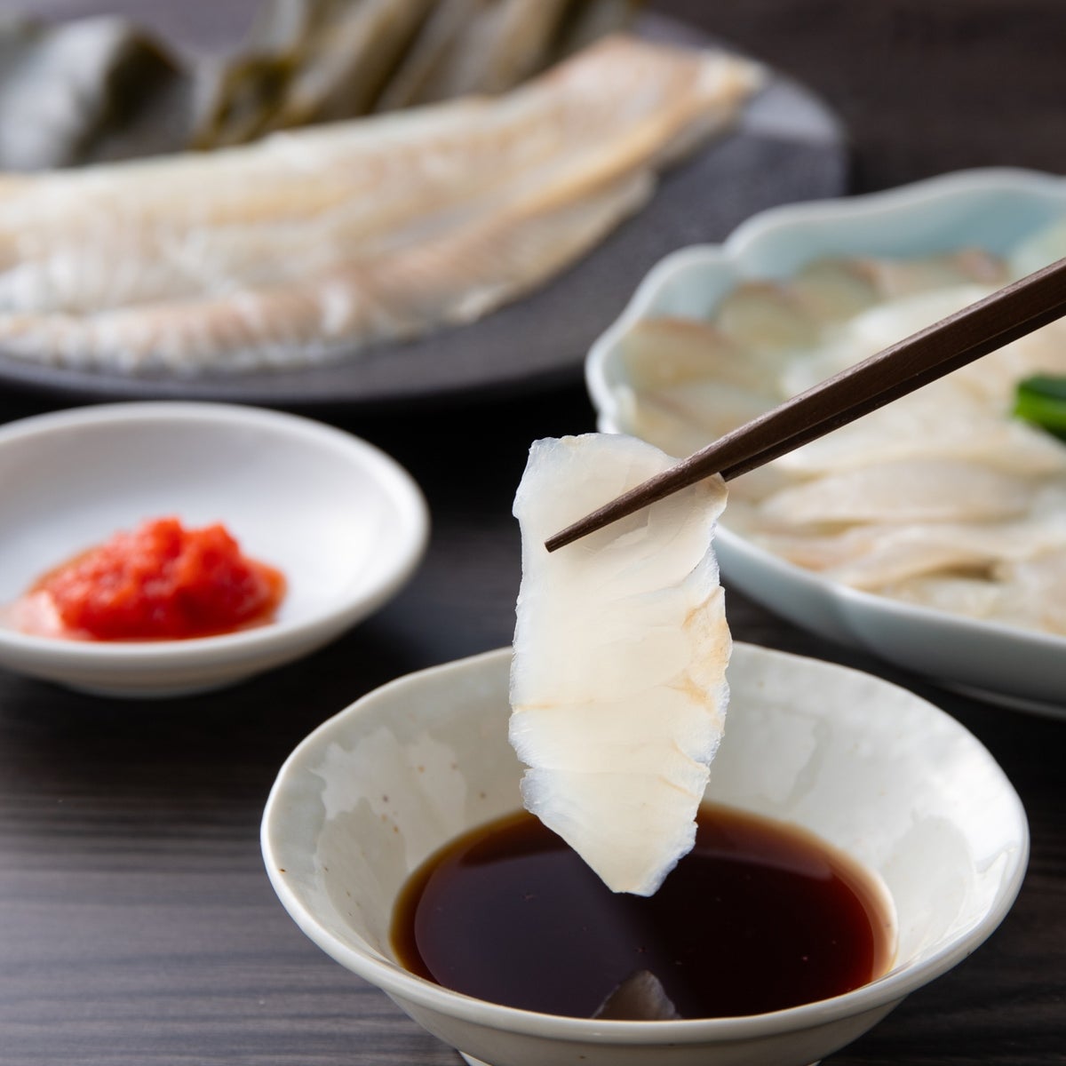 箸で持ち上げたかぼすヒラメの刺身を特製ポン酢にくぐらせる瞬間。弾力のある身の質感と上品な脂ののりが伝わるシズル写真。