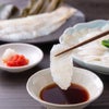 箸で持ち上げたかぼすヒラメの刺身を特製ポン酢にくぐらせる瞬間。弾力のある身の質感と上品な脂ののりが伝わるシズル写真。