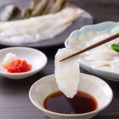 箸で持ち上げたかぼすヒラメの刺身を特製ポン酢にくぐらせる瞬間。弾力のある身の質感と上品な脂ののりが伝わるシズル写真。