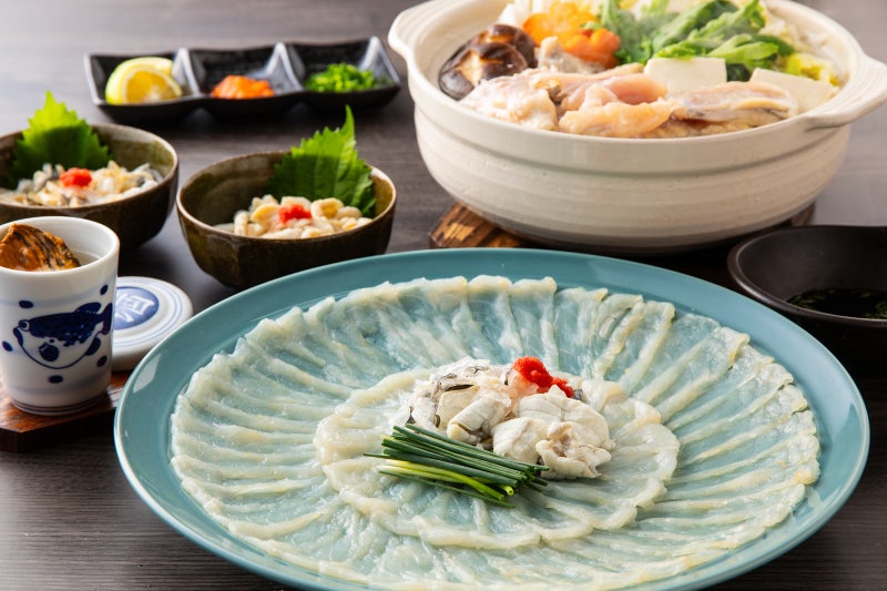 大分ブランド「豊後とらふぐ」を家庭で味わい尽くす豪華フルコースの食卓風景。美しく引かれたとらふぐ刺身（てっさ）の大皿を中心に、ふぐちり鍋や皮刺し、ひれ酒が並ぶ贅沢なイメージ。